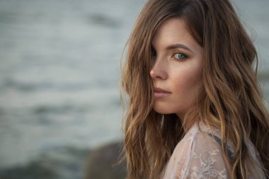 Açık havada esintili kahverengi saçlı genç bir kadının yakın plan portresi.