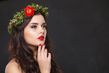 Çiçekli baş çelengi ile siyah arka planda poz veren çekici genç bir kadın.