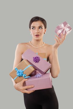 Tatiller, kutlamalar ve kadın konsepti. Mutlu esmer mankenin portresi hediye kutusunu sallıyor içinde doğum gününü kutlarken ne olduğunu merak ediyor gri arka planda doğum günü hediyeleri alıyor.