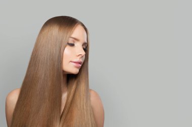 Modern makyajlı ve uzun düz saç stili beyaz stüdyo arka planında duran zarif genç kadın modeli.