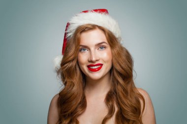 Makyajlı ve güzel gülümseyen Noel Baba şapkalı muhteşem bir kadın kameraya, moda resmine bakıyor.
