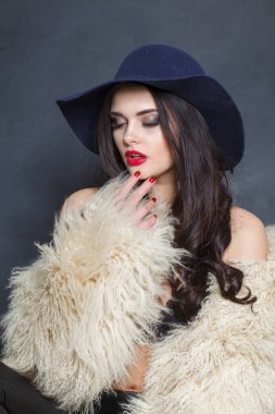 Kırmızı dudaklı, uzun dalgalı saçlı, mavi şapkalı, koyu renk stüdyo arka planlı güzel bir kadın.