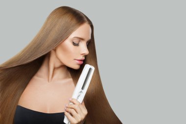Beyaz arka planda düzeltici demir kullanan uzun, düzgün, sağlıklı saç stili olan büyüleyici, gülümseyen bir kadın. Güzellik, saç bakımı, saç bakımı ve kozmetik konsepti