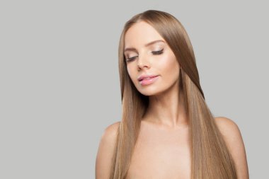 Güzel kadın yüzü. Gri arka planda uzun kahverengi saçlı ve makyajlı bir model. Güzellik, saç bakımı ve kozmetik portre