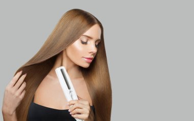 Uzun kahverengi düz saç stili, düz demir tutan genç kadın modelinin yakın plan portresi. Kuaför, güzellik bakımı, saç düzleştirme, makyaj ve stil.