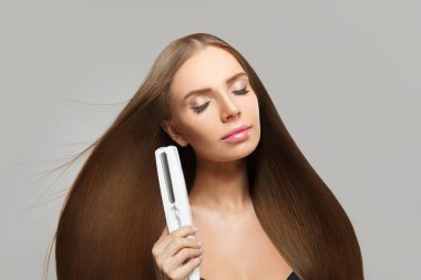 Beyaz arka planda düzeltici demir kullanan, uzun, düz, sağlıklı saç stili mükemmel bir kadın. Güzellik, saç bakımı, saç bakımı ve kozmetik konsepti