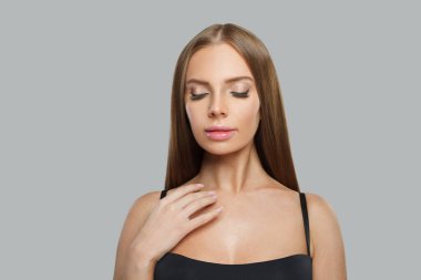 Genç kadın yüzü. Gri arka planda uzun kahverengi saçlı ve makyajlı bir model. Güzellik, saç bakımı ve kozmetik portre