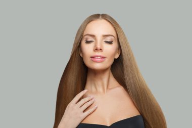 Mutlu kadın yüzü. Gri arka planda uzun kahverengi saçlı ve makyajlı bir model. Güzellik, saç bakımı ve kozmetik portre