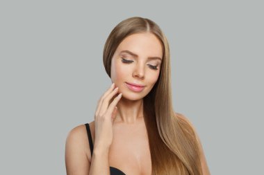 Şirin kadın suratı. Gri arka planda uzun kahverengi saçlı ve makyajlı bir model. Güzellik, saç bakımı ve kozmetik portre