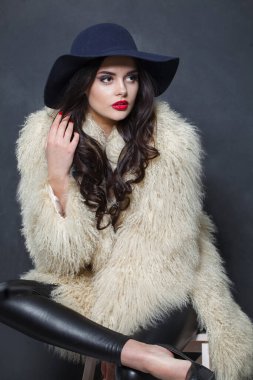 Mavi şapkalı, beyaz kürklü, iç mekanda poz veren model kadın, zarif moda güzellik portresi.