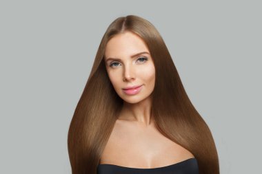 Neşeli kadın yüzü. Gri arka planda uzun kahverengi saçlı ve makyajlı bir model. Güzellik, saç bakımı ve kozmetik portre