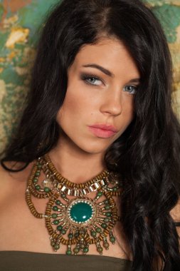 Sanat stüdyosunda poz veren çekici esmer kadın. Uzun kıvırcık saçlı ve yeşil arka planda makyajlı genç bayan.