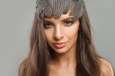 Sağlıklı, uzun, dalgalı saç stili, modaya uygun makyaj ve kafasındaki aksesuar aksesuarları kameraya, moda güzelliği portresine bakan çekici bir kadın modeli.