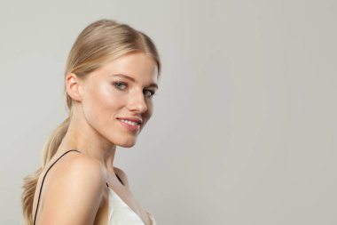Çekici, genç, sarışın, açık tenli, yumuşak makyajlı, sağlıklı saçlı ve doğal duygusal ifade portresi olan bir manken. Beyaz arka planda sarışın kadın.