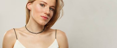 Açık tenli, yumuşak makyajlı, sağlıklı saçlı ve doğal duygusal ifade portresi olan genç sarışın kadın modelin yakın plan portresi. Beyaz arka planda sarışın kadın.