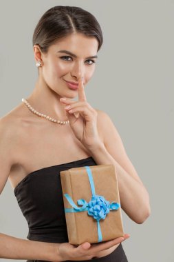 Gri stüdyo arka planında hediye kutusunu tutan genç ve güzel bir kadın. Moda güzelliği portresi.