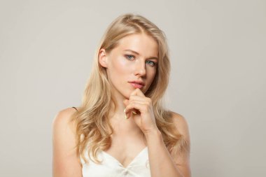 Açık tenli, yumuşak makyajlı, sağlıklı saçlı ve doğal duygusal yüz ifadesi olan genç, dalgın bir manken. Beyaz arka planda sarışın kadın.