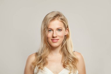 Çekici, genç, sarışın, açık tenli, yumuşak makyajlı, sağlıklı saçlı ve doğal duygusal yüz ifadesi olan bir manken. Beyaz arka planda sarışın kadın.