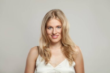 Gülümseyen genç sarışın kadın model, açık tenli, yumuşak makyajlı, sağlıklı saçlı ve doğal duygusal yüz resmi olan. Beyaz arka planda sarışın kadın.