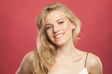 Açık tenli, yumuşak makyajlı, sağlıklı saçlı ve doğal duygusal yüz ifadesi olan genç bir model. Kırmızı arka planda sarışın kadın.