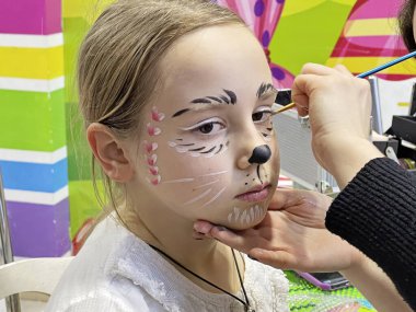 Makyaj sanatçısı yaratıcı karnaval makyajını yaparken tatlı esmer kız oturuyor. 