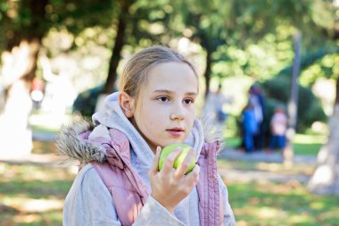 Yeşil elma tutan neşeli çocuk. Parkta genç bir kız, açık hava portresi.