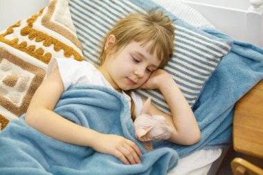 Şirin bir çocuk evdeki yatağında kedi evcil hayvanıyla kestiriyor. Sevimli, tatlı, küçük bir kızın ev portresi.