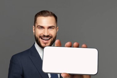 Gri arka planda, boş telefon ekranı olan başarılı iş adamının portresi