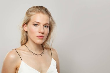 Açık tenli, yumuşak makyajlı, sağlıklı saçlı ve doğal duygusal yüz ifadesi pozu veren genç sarışın bir manken. Beyaz arka planda sarışın kadın.