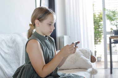 Akıllı telefonlu konsantre küçük kız çizgi film izliyor ya da evde mobil oyunlar oynuyor, kapalı alanda portre yapıyor.