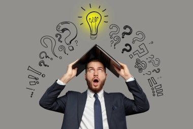 Duygusal şokta olan takım elbiseli iş adamı kafasında dizüstü bilgisayarla gri arka planda ampul ve soru işaretleri çiziyor.