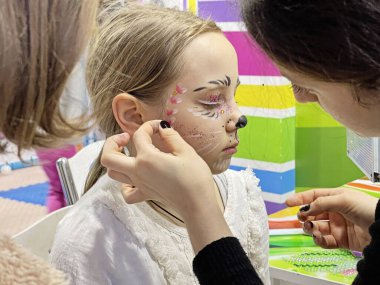 Esmer kız makyaj sanatçısı yaratıcı karnaval makyajını yaparken oturuyor. 