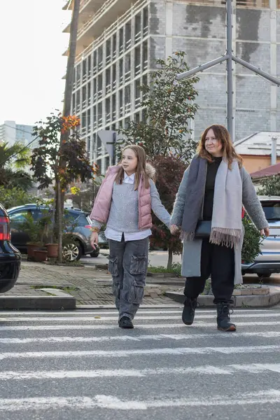 Mutlu anne ve kız birbirlerinin elini tutup yaya geçidinden karşıya geçiyorlar.