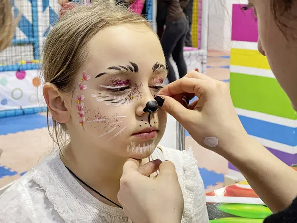 Makyaj sanatçısı yaratıcı karnaval makyajını yaparken çocuk oturuyor. 