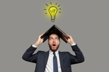 Duygusal şokta olan takım elbiseli bir iş adamı kafasında dizüstü bilgisayarla gri arka planda, kafasının üstünde sarı bir ampul var. Fikir kavramı