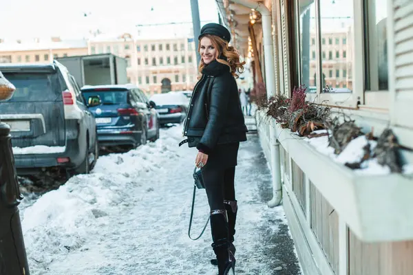 Kış şehrinin arka planında duran siyah deri ceketli gülümseyen esmer kadın.