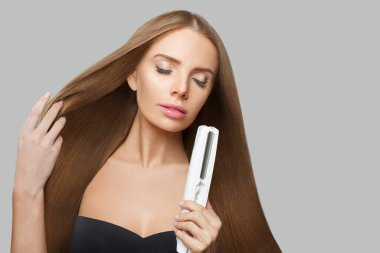 Beyaz arka planda saç düzleştirici kullanan görkemli manken kadın. Harstyle, saç bakımı, güzellik salonu ve tedavi konsepti