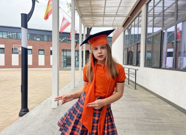 Mezuniyet şapkalı ve okul üniformalı mutlu çocuk okul bahçesinde eğleniyor. Eğitim ve mezuniyet kavramı