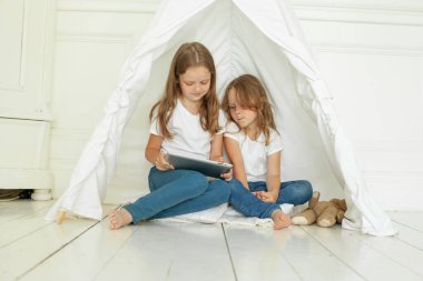 Evde tablet bilgisayar kullanan neşeli kız kardeşler.