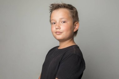 Siyah tişörtlü yakışıklı okul çocuğu beyaz arka planda kameraya bakıyor.