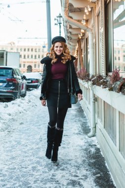 Kış şehrinin arka planında duran siyah deri ceketli ve topuklu ayakkabı giyen çekici esmer kadın. 