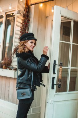 Gülümseyen esmer, siyah deri ceketli, mavi çantalı kadın dükkana gidiyor..