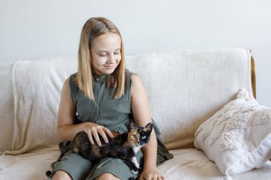 Evcil kedisine sarılan genç bir kızın portresi rahat bir kanepede oturmuş, evde dinleniyor. Çocuk ve evcil kedi evde. Aşk, bağlılık ve ev hayatı kavramı.