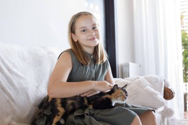 Güzel genç kız kedi evcil hayvanını kucaklıyor rahat bir kanepede oturuyor, evde dinleniyor. Çocuk ve evcil kedi evde. Aşk, bağlılık ve ev hayatı kavramı.