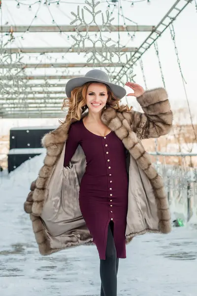 Güzel esmer kadın Kar Şehri caddesinde yürüyor. Şapkalı, kırmızı elbiseli ve kürklü..