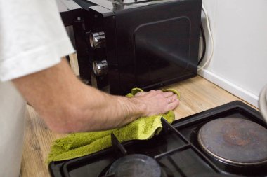 Adam mutfak üstünü temizliyor, eli yeşil paçavrayla yakın plan.