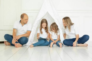 Anne, baba ve çocuklar evdeki oturma odasında tablet alet kullanıyorlar. Mutlu aile