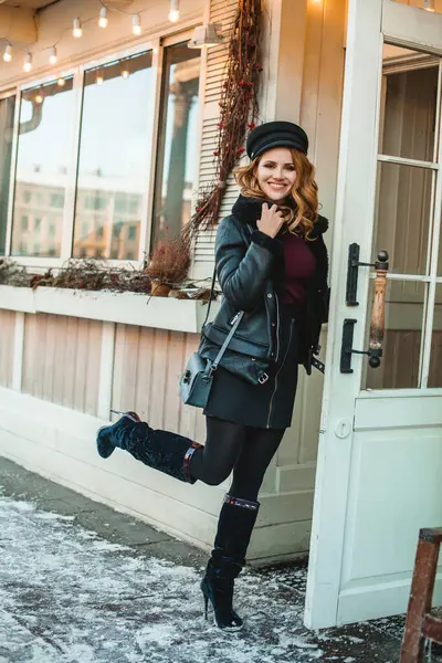 Siyah deri ceketli, mavi çantalı, gülümseyen esmer kadın dükkan kapısının yanında duruyordu.