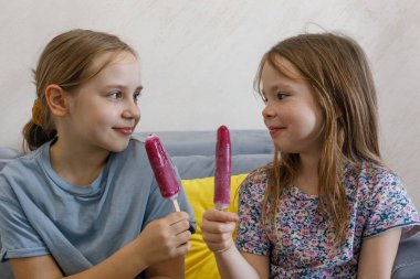 Çocuklar Evdeki rahat bir oturma odasında bir koltukta otururken dondurmanın tadını çıkarıyorlar..