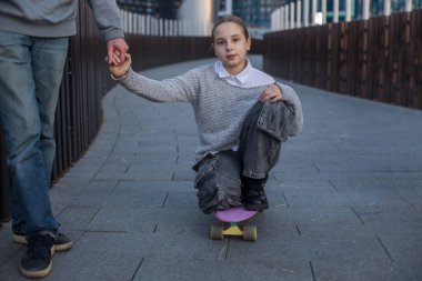 Destek, güvenlik ve aile kavramı. Kaykaylı bir kız çocuğu ailesinin elini tutuyor..